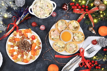 Christmas new year dishes, traditional festive salad olivier and cheese with tomatoes, grapes and honey with fir branches and cones and decorations, dish design idea,