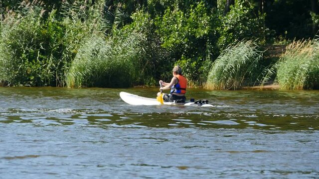 teenager in life jacket with paddle on windsurf board slow motion