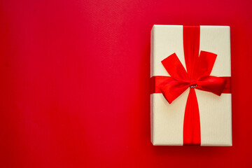 A white gift box with a red ribbon on a red background. Flat lay.
