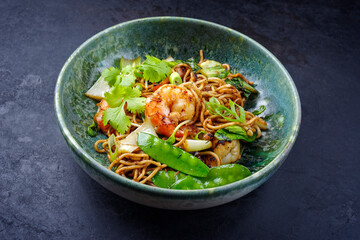 Modern style traditional stir-fried Thai phak kung with king prawns, vegetable and noodles served as close-up in a Nordic design bowl