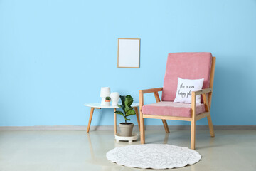 Comfy armchair with table and rug near color wall in interior of room