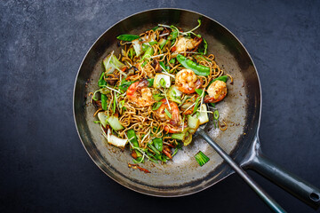 Traditional stir-fried Thai phak kung with king prawns, vegetable and noodles served as top view in a classic design wok - obrazy, fototapety, plakaty