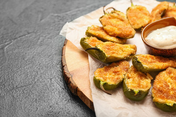 Board with tasty jalapeno poppers with sauce on dark background, closeup