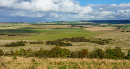 Fototapeta premium a view over woodland and meadows East of Everleigh from Sidbury Hill, WIltshire (Historical landmark) under a blue and white cloud sky