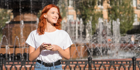 A beautiful, attractive and happy redhead Caucasian girl using a smartphone. Freelance concept.