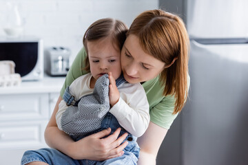 Woman hugging daughter with down syndrome in baking glove in kitchen.