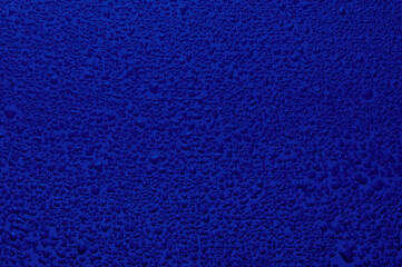 Water drops on black glass. Background illuminated with dark blue ​light.