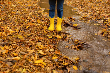 children's feet in yellow boots stand in the autumn forest next to the river