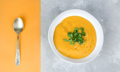 Orange cream soup. Pumpkin or lentil puree soup on concrete background and spoon on orange background