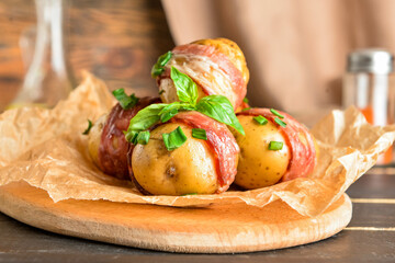 Wooden board of tasty baked potatoes with bacon on table