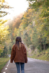 back girl walking with a brown coat in autumn in a road to a green and brown trees forest