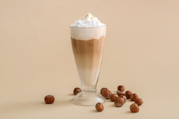 Glass of tasty latte with nuts on beige background