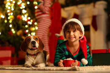 Little boy with cup of hot cocoa and cute dog at home on Christmas eve