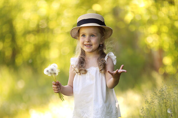summer portrait of a little beautiful curly girl in a straw hat blowing dandelions. allergy free concept.