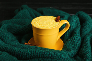 Cup of tasty turmeric latte and sweater on table