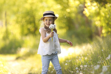 summer portrait of a little beautiful curly girl in a straw hat blowing dandelions. allergy free concept.