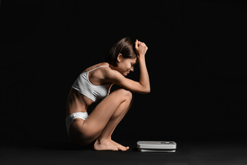 Young woman with scales on dark background. Anorexia concept