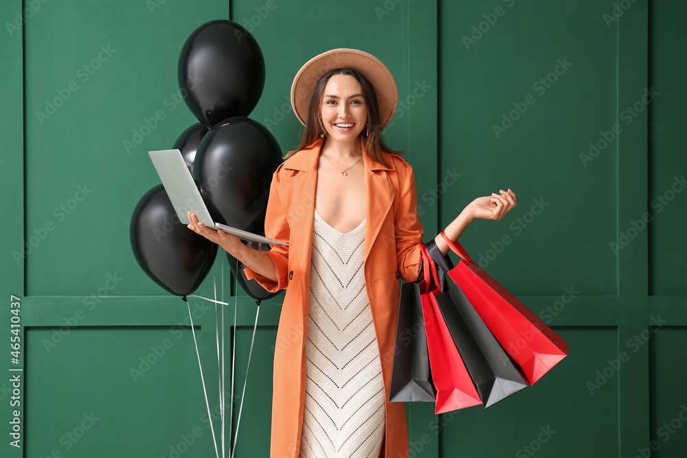 Sticker Happy young woman with laptop and shopping bags on color background. Black Friday sale