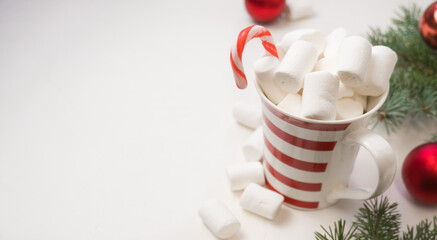 hot chocolate with marshmallows in a red and white bakery on a white background and branches of a New Year tree.