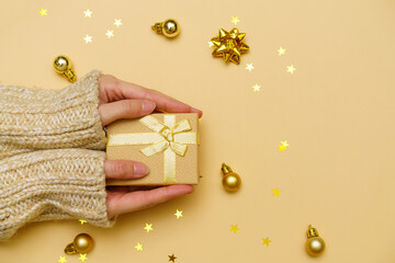 Female hands in sweater hold gift or gift box decorated with confetti and christmas balls on a...