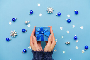 Balls and snowflakes and new year's gift in hands of woman in dark sweater on blue background....