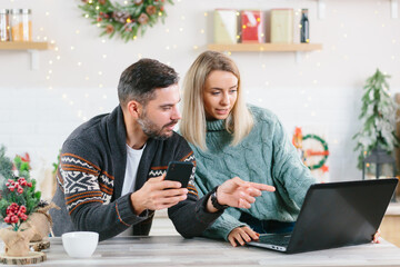 Young couple husband and wife working together online at home, with laptop sitting in the kitchen, happy together, during the New Year and Christmas holidays