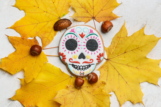Skull shaped cookie for Mexico's Day of the Dead (El Dia de Muertos) with nuts and fallen leaves on white background
