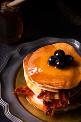 Fresh homemade pancake stack with crispy organic bacon and blueberry fruit butter drippings honey maple syrup for tasty sweet morning breakfast with American traditional authentic style