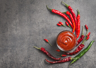 Spicy sauce or hot ketchup copy space dark background top view.Red sauce ketchup in bowl and fresh chili peppers.