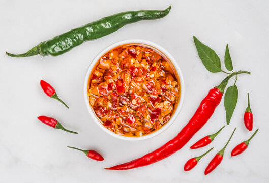 Chili hot peppers oil sauce seasoning and fresh chili peppers red and green on white marble background copy space.