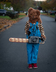 Child with scary Halloween costume of bear mask and chainsaw