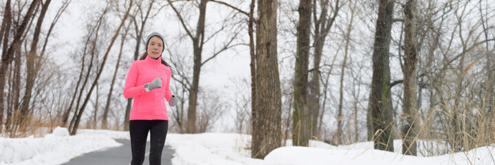 Winter exercise Asian runner girl running on snow trail in forest park. Panoramic banner of fitness...