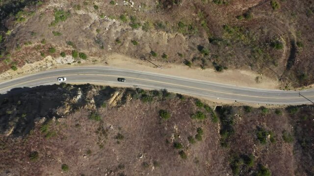 Top down shot of exotic performance cars racing down road on sunny summer day, California USA 4K. Overhead aerial new sport cars driving zigzag by empty mountain highway road in Malibu canyon mountain
