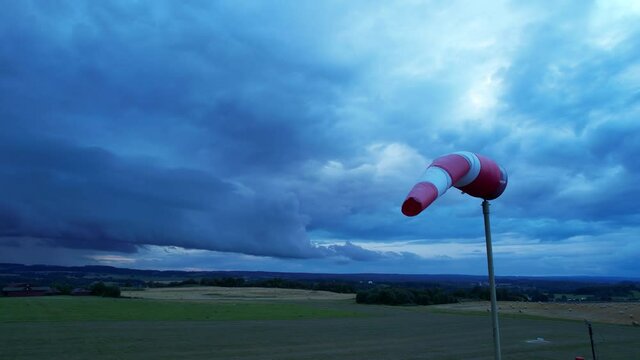 White-red airport windsock is blown by the wind against a stormy sky.