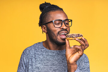 Diet concept. Hungry african american black bearded man eating donut isolated over yellow...