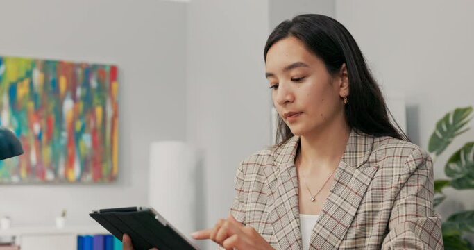 A conscientious organized office worker in a large corporation sits at desk synchronizing documents on tablet with computer, comparing data, clicking the screen, scrolling, focused on her work