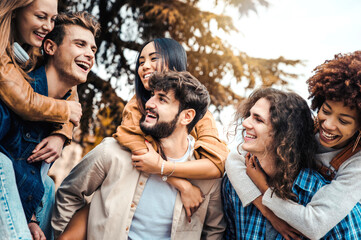 Millennials friends on vacation having piggyback race on city street - Young people group enjoying time together laughing outdoors - Summer vacations, friendship and happy lifestyle concept - Powered by Adobe