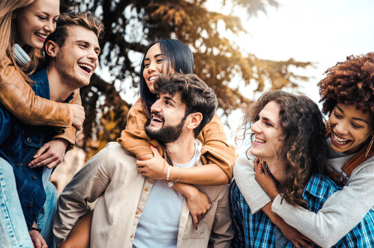 Millennials friends on vacation having piggyback race on city street - Young people group enjoying time together laughing outdoors - Summer vacations, friendship and happy lifestyle concept