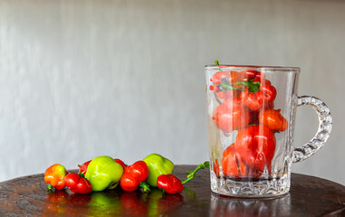Ripe green and red spicy cherry peppers inside the glass cup on wooden base.