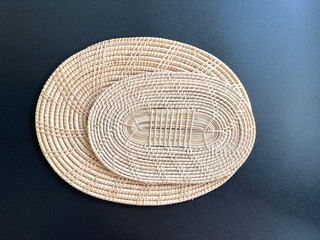 Oval shaped woven rattan placemat on black background, handmade kitchenware, weave craft product