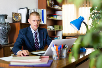 Experienced american businessman sitting in office at workplace and working at laptop