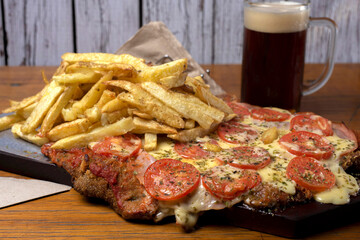 Neapolitan Milanese with mozzarella and sliced tomato garnished with French fries and beer on wooden board