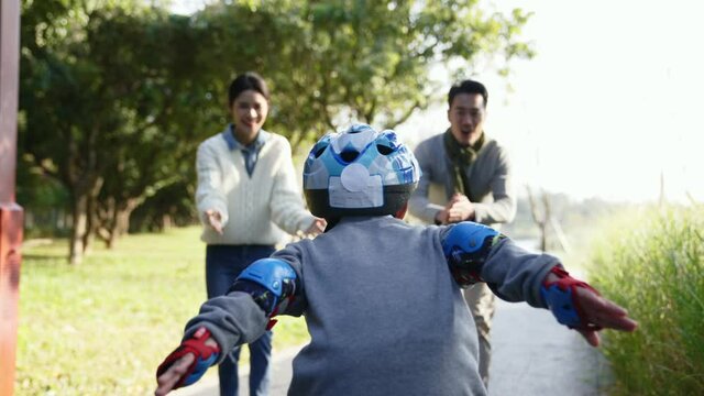 little asian boy learning roller skating outdoors encouraged by parents