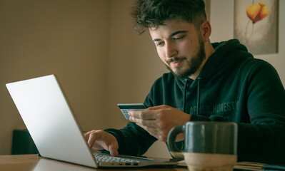 young man making online purchases with a card in front of a laptop