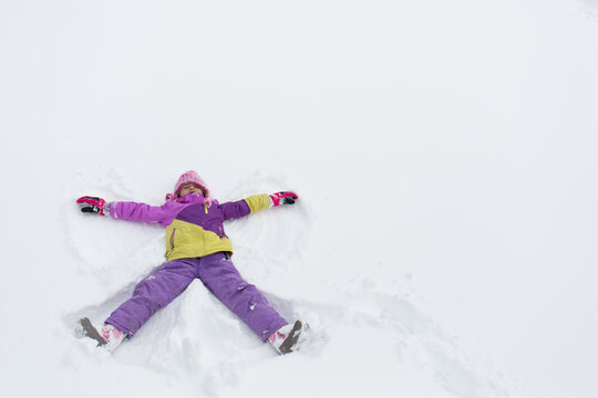 Young girl wearing snowpants and jacket making a snow angel in the winter snow