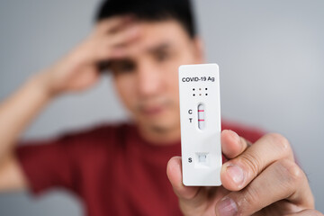 stressed man holding Coronavirus(Covid-19) positive test result with Antigen Rapid Test kit (ATK)
