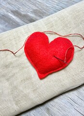 red textile heart with needle on beige fabric