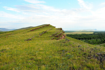 Layered rock formations on top of a high hill overlooking a picturesque valley.