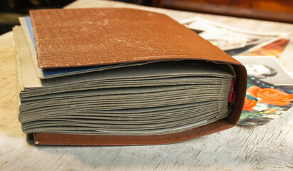 a worn photo album with gray sheets and a brown cover, postcards and photos are lying next to it