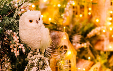 The toy owl sits on the background of toy wooden houses decorated with glowing garlands. New Year' decoration